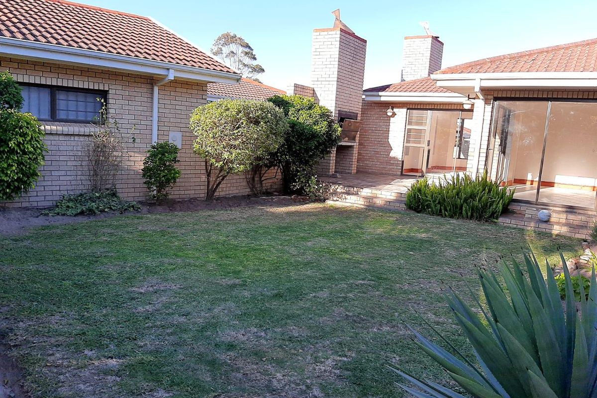 Rear exterior view of the townhouse featuring a private garden, paved patio area with a built-in braai, and sliding door access to the interior.