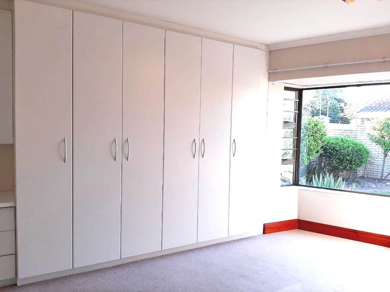 A bright, empty bedroom featuring extensive floor-to-ceiling built-in cupboards and a large bay window overlooking the garden.
