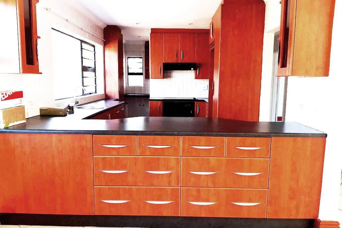 A functional kitchen featuring warm-toned laminate cabinetry, dark countertops, built-in oven, extractor fan, and tiled flooring, offering a practical layout for daily use.