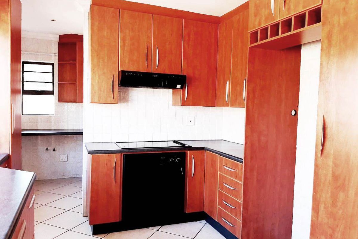 A functional kitchen featuring wooden cabinetry, dark countertops, an electric hob with extractor fan, and tiled flooring, offering a clean and practical workspace.