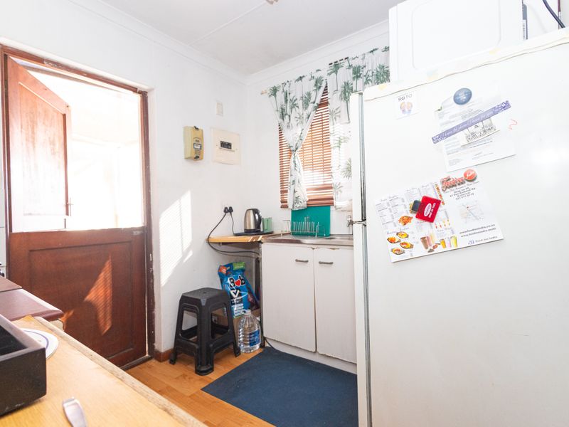 A compact kitchen area featuring basic cabinetry, a sink, timber flooring, and direct access to an exterior door.