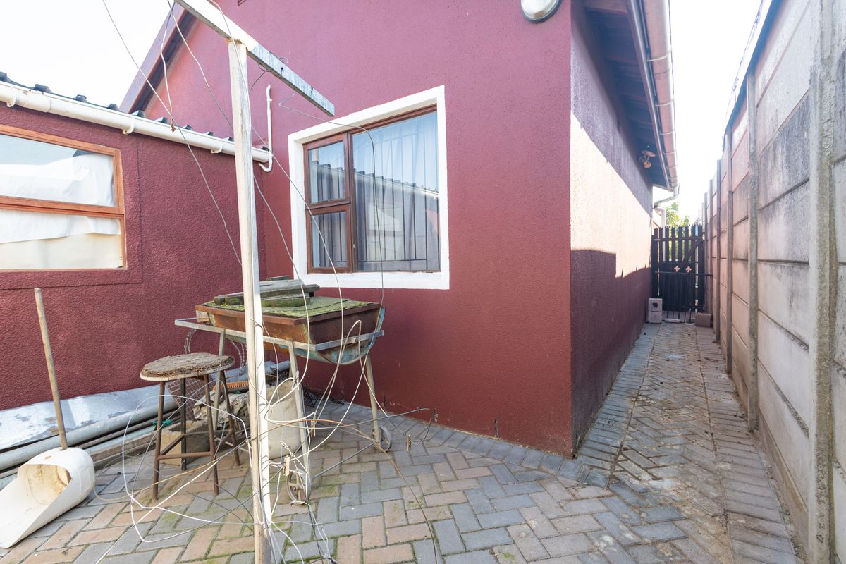 A narrow paved side passage along the rear exterior of the house, featuring a security gate and perimeter walling.