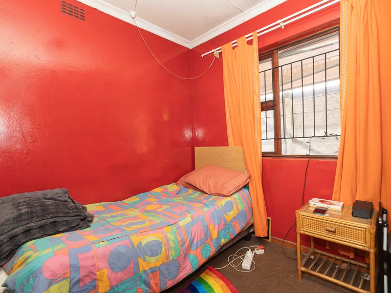 A compact bedroom featuring security bars on the window and a simple layout, currently finished with bold wall paint.