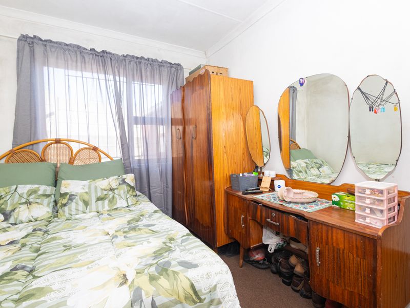 A bedroom featuring a window with curtains and coving, showing signs of wear on the walls.