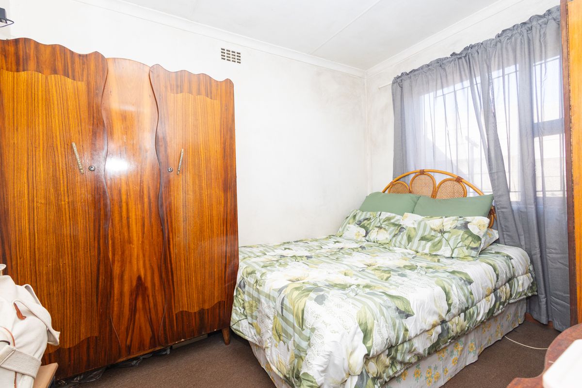 A bedroom featuring a window with security bars, coving, and a built-in ventilation vent, showing signs of wear on the wall surfaces.