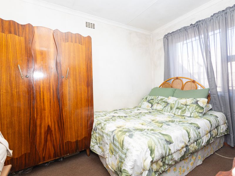 A bedroom featuring a window with security bars, coving, and a built-in ventilation vent, showing signs of wear on the wall surfaces.