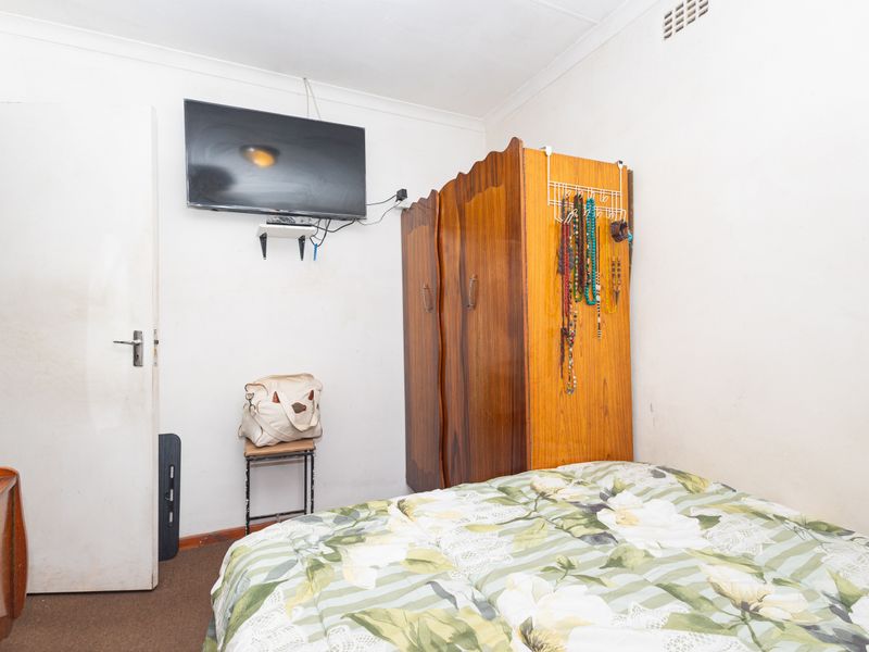 A compact bedroom featuring neutral walls and carpeted flooring, providing a functional space for rest.