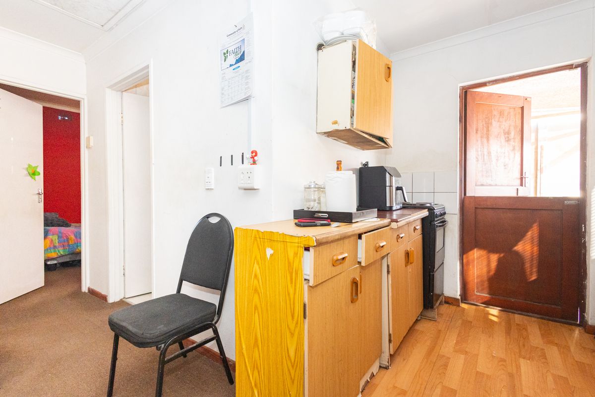 A compact kitchen area featuring dated timber cabinetry, laminate countertops, and a tiled splashback, with direct access to an exterior door.