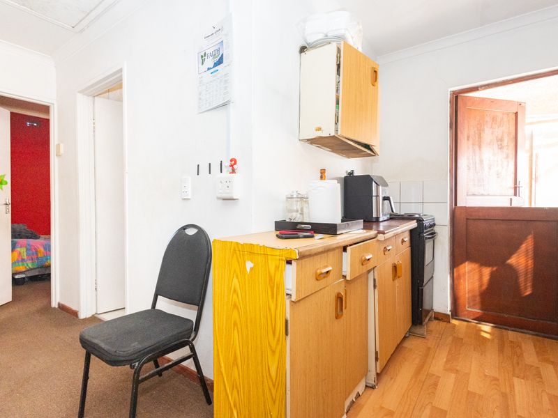 A compact kitchen area featuring dated timber cabinetry, laminate countertops, and a tiled splashback, with direct access to an exterior door.