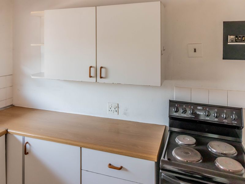 A functional kitchen area featuring built-in cabinetry, laminate countertops, a tiled splashback, and a freestanding electric stove.