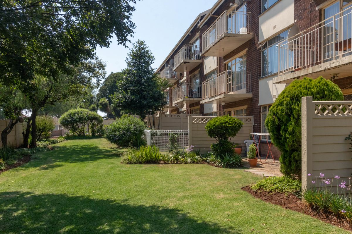 Rear view of a multi-story apartment building featuring brick facade, private balconies with metal railings, and a well-maintained communal garden area.