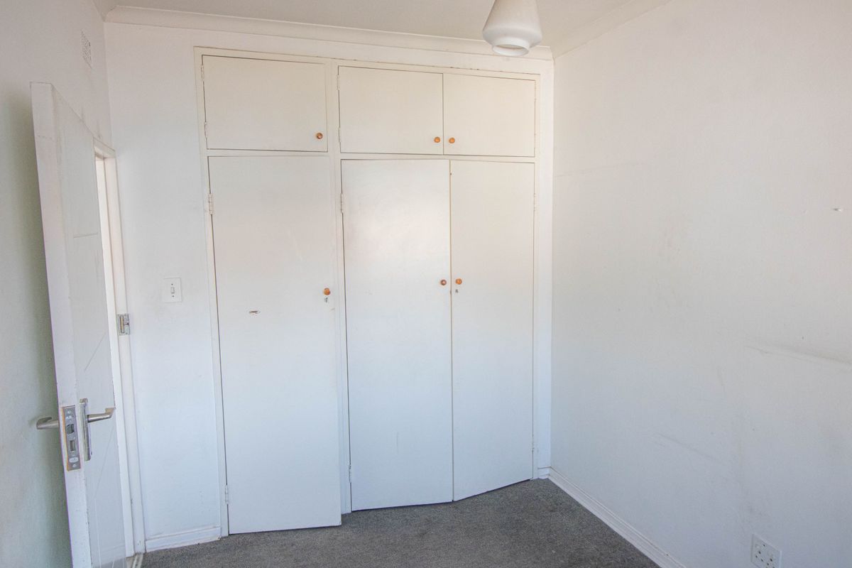 An empty bedroom featuring built-in cupboards with overhead storage and carpeted flooring, requiring minor cosmetic updates to refresh the space.