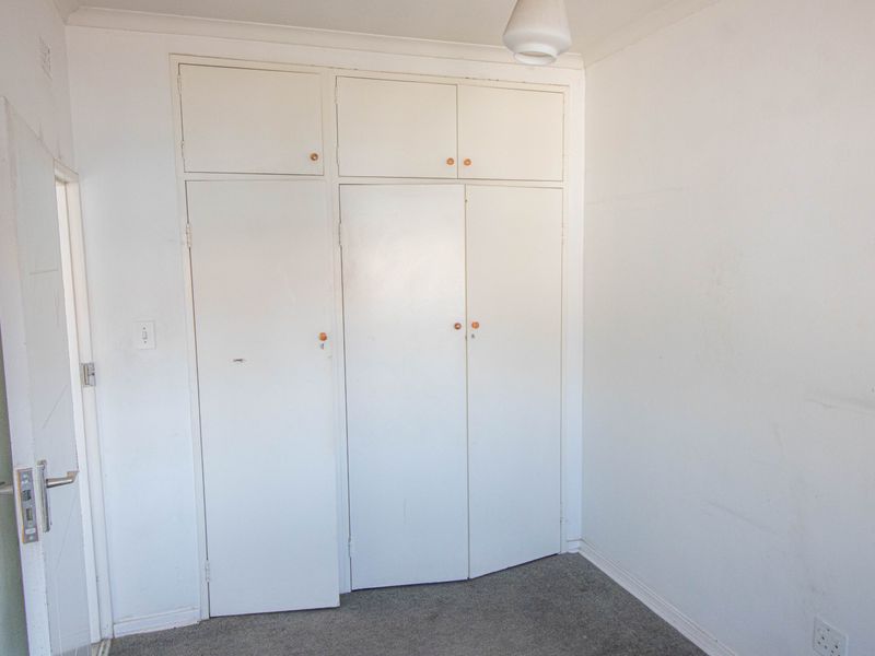 An empty bedroom featuring built-in cupboards with overhead storage and carpeted flooring, requiring minor cosmetic updates to refresh the space.