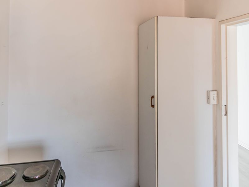 A compact kitchen area featuring a built-in storage cupboard and an electric stove, requiring minor cosmetic updates to improve its overall appearance.