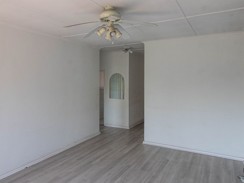 An empty living room featuring light-toned laminate flooring, a ceiling fan, and a coved ceiling, leading into an adjacent hallway area.
