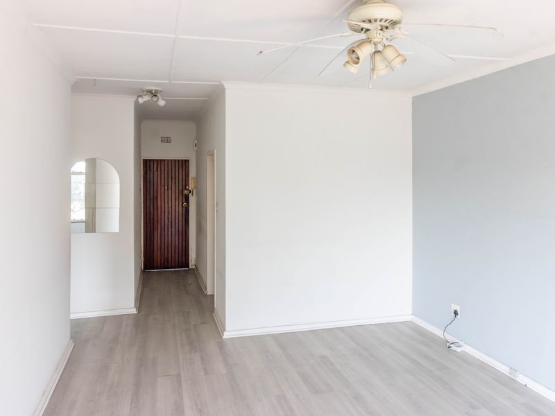 An empty living area featuring light-toned laminate flooring, a ceiling fan, and a classic timber entrance door.