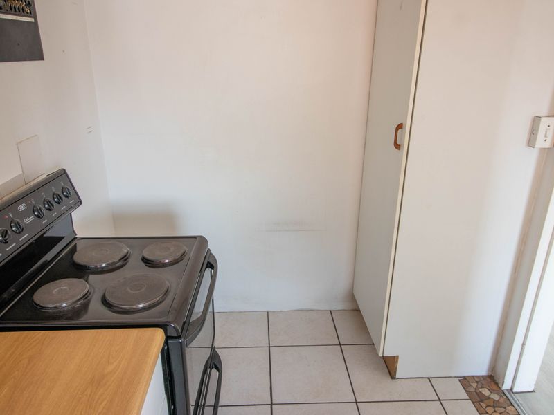 A compact kitchen area featuring a freestanding stove, tiled flooring, and a built-in storage cupboard.