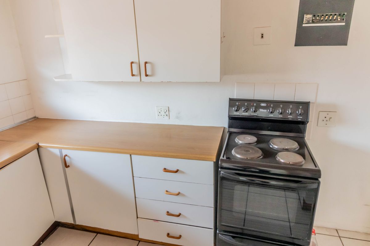 A compact kitchen featuring white cabinetry, laminate countertops, and a freestanding electric stove, offering a functional space ready for modernization.