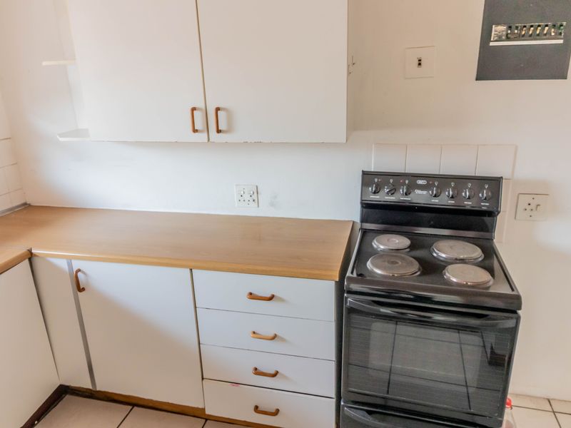 A compact kitchen featuring white cabinetry, laminate countertops, and a freestanding electric stove, offering a functional space ready for modernization.