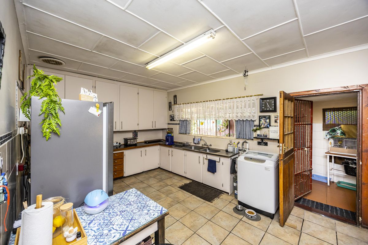A functional kitchen featuring built-in cabinetry, double basin sink, and tiled flooring, with an adjacent utility area accessible through a security gate.