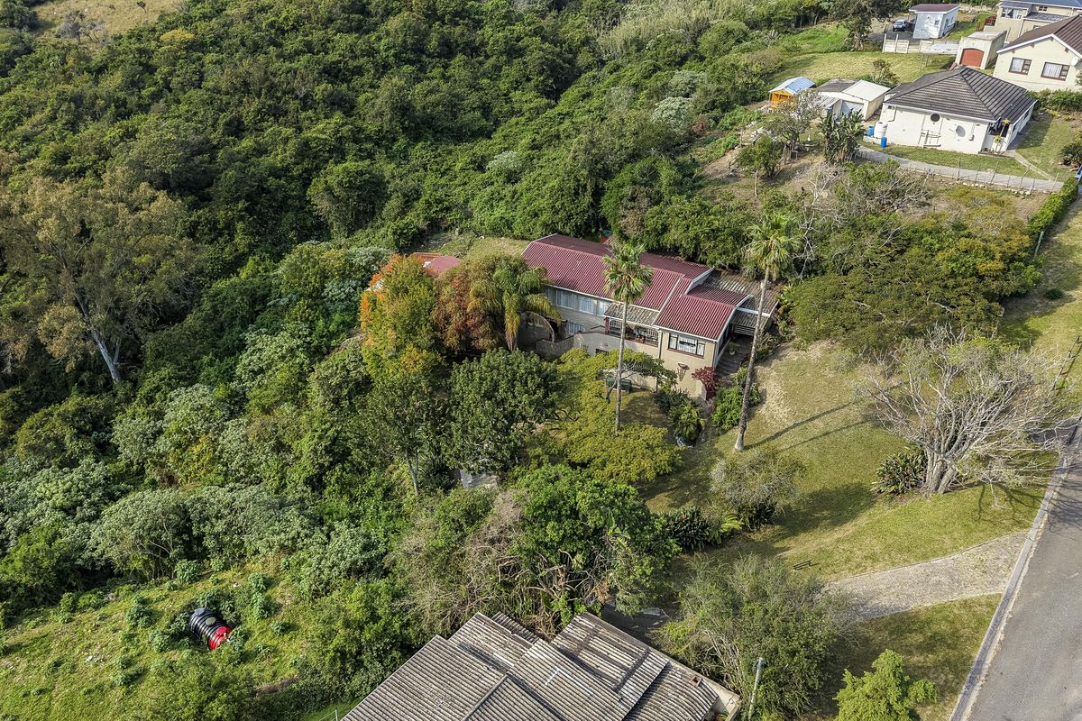 Aerial view of a residential property featuring a metal roof, established garden, and paved driveway, situated in a lush, green environment.