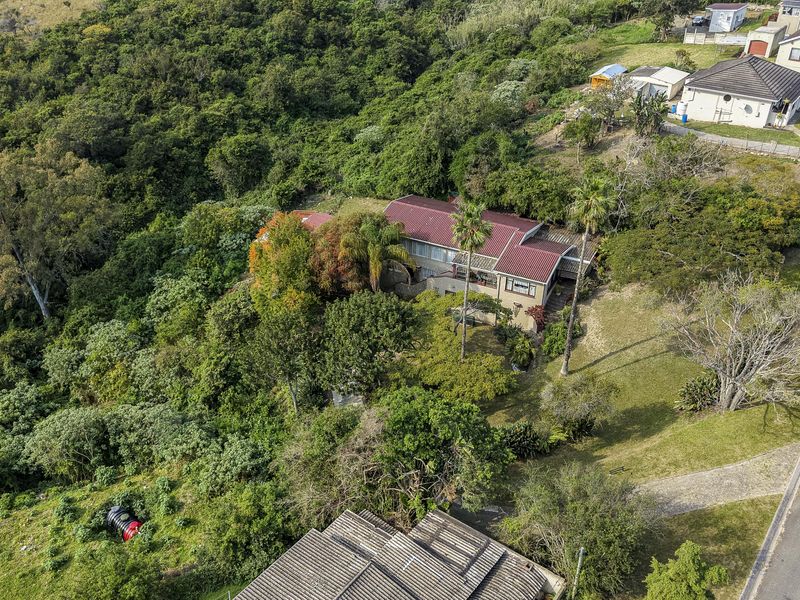 Aerial view of a residential property featuring a metal roof, established garden, and paved driveway, situated in a lush, green environment.