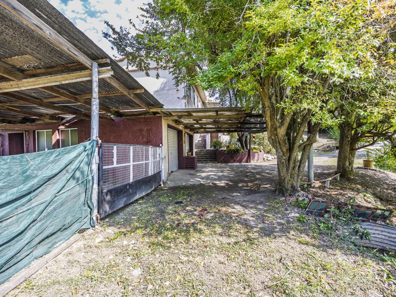 Rear exterior view showing a concrete driveway, metal gate, and a weathered structure with a corrugated iron roof.