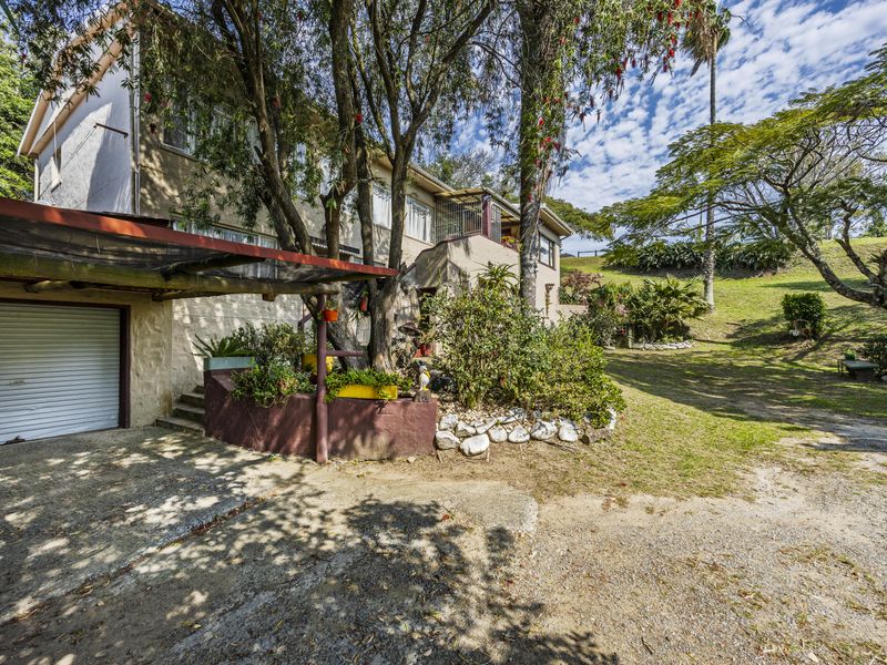 Rear view of the property featuring a garage, concrete driveway, and a spacious, established garden area with mature trees.