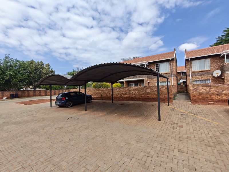 Exterior view of the apartment complex featuring a covered carport, brick paved driveway, and facebrick facade with tiled roofing.