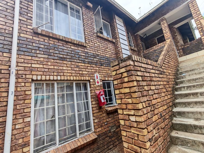 Exterior view of a face brick apartment building featuring a concrete staircase and steel-framed windows.