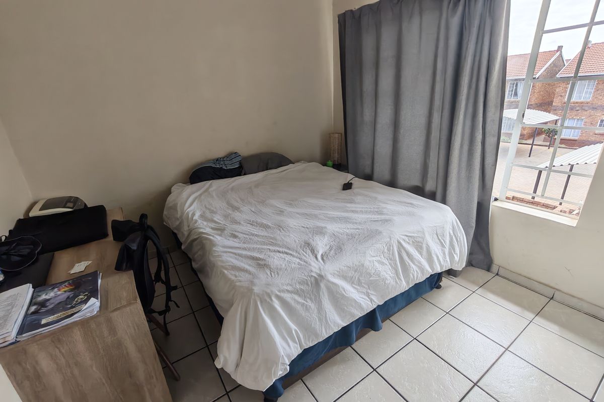 A functional bedroom featuring tiled flooring and a large window providing natural light and views of the complex.