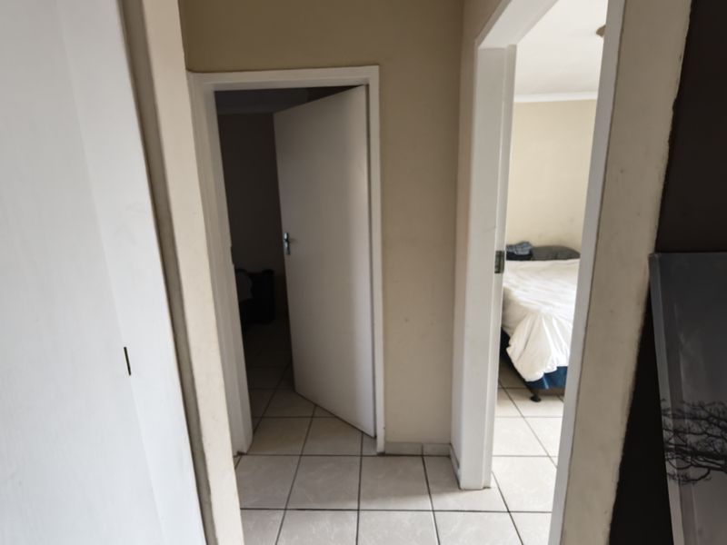 A functional hallway area featuring tiled flooring and access to adjacent rooms, showing signs of wear and requiring cosmetic updates.