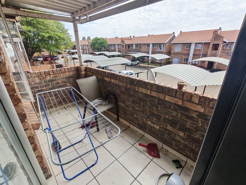A functional balcony featuring a brick balustrade, tiled flooring, and a corrugated metal roof covering, overlooking the complex parking area.