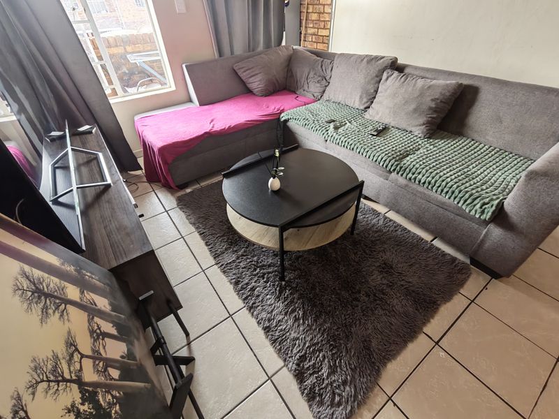 A living room area featuring tiled flooring and a large window, providing natural light to the space.