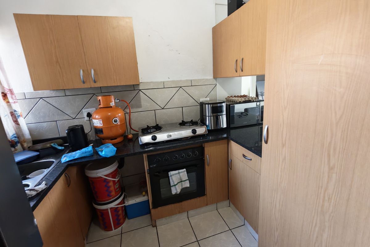 Compact kitchen featuring laminate cabinetry, granite countertops, a built-in oven, gas hob, and tiled backsplash, requiring some cosmetic updates.