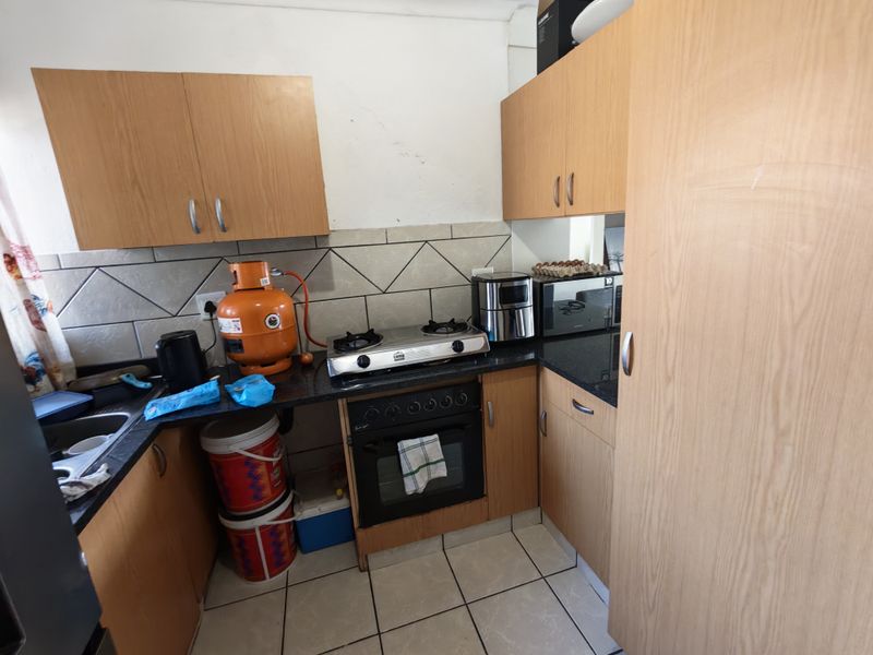 Compact kitchen featuring laminate cabinetry, granite countertops, a built-in oven, gas hob, and tiled backsplash, requiring some cosmetic updates.