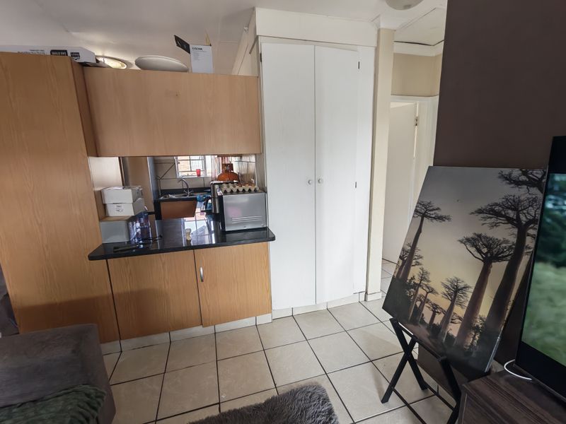 A compact kitchen area featuring laminate cabinetry, granite countertops, a stainless steel sink, and tiled flooring, with an adjacent built-in pantry cupboard.
