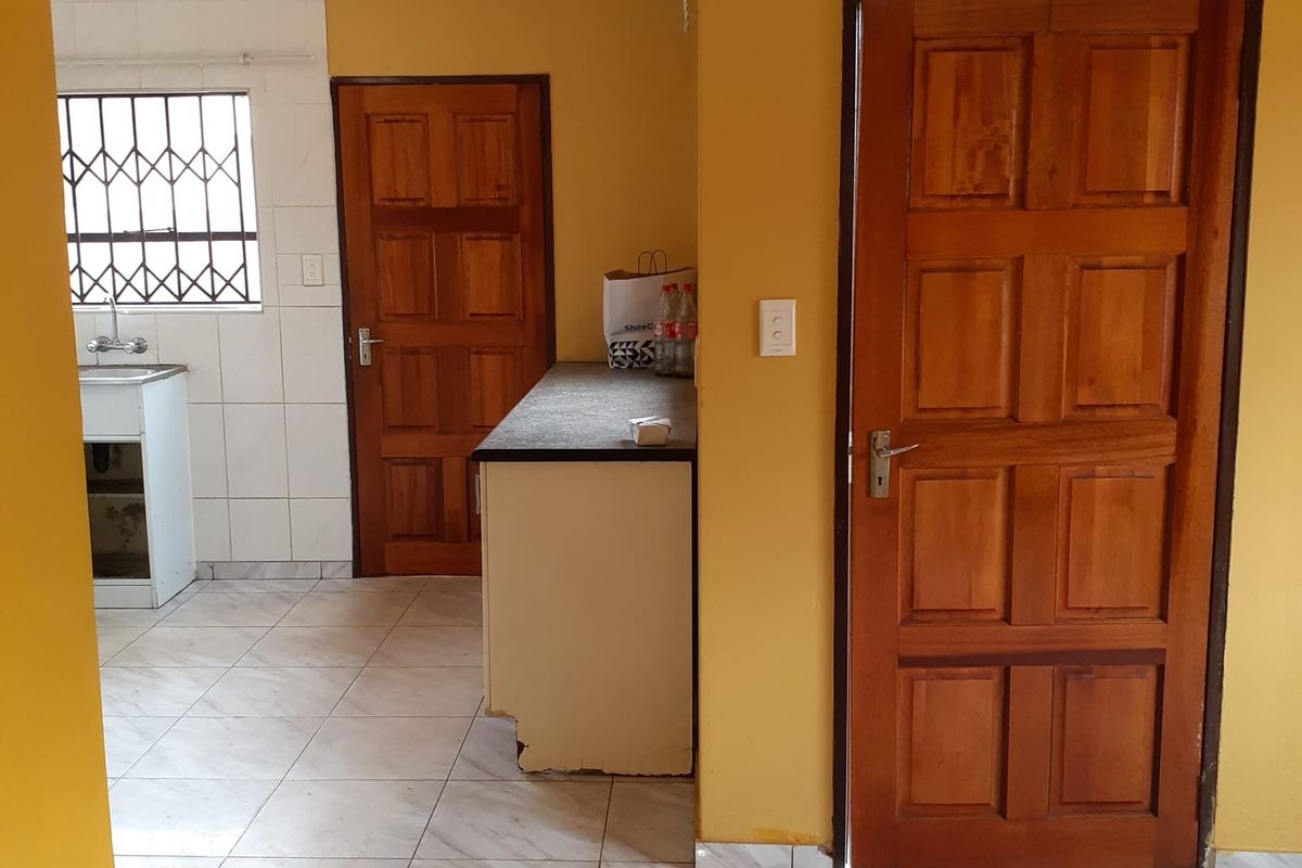 A functional kitchen area featuring tiled floors, built-in cabinetry with a sink, and wooden doors, presenting a dated but practical office utility space.