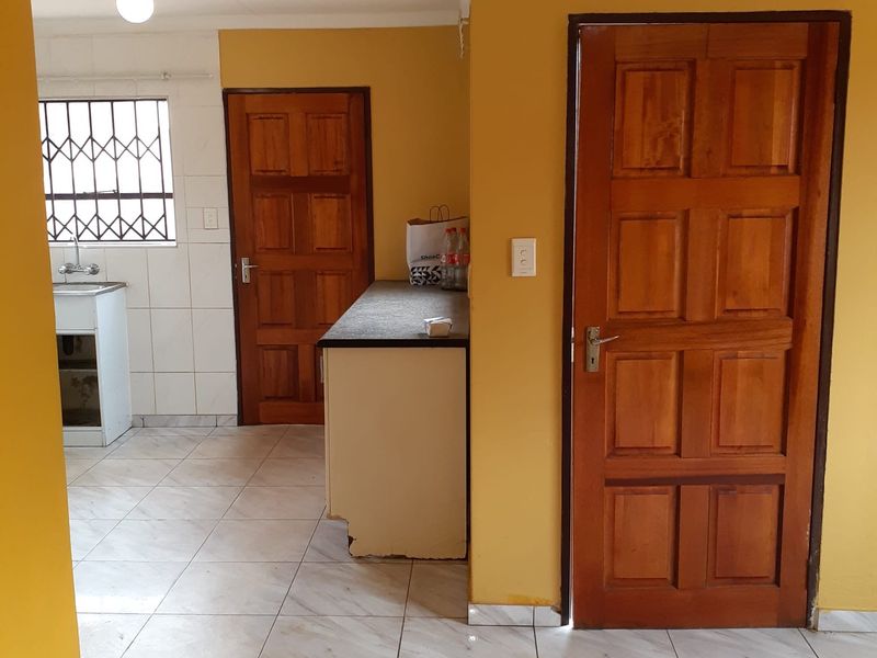 A functional kitchen area featuring tiled floors, built-in cabinetry with a sink, and wooden doors, presenting a dated but practical office utility space.