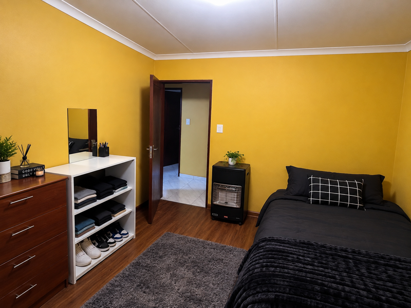 A functional office space featuring laminate flooring, coved ceilings, and a bright yellow accent wall, currently utilized as a bedroom.