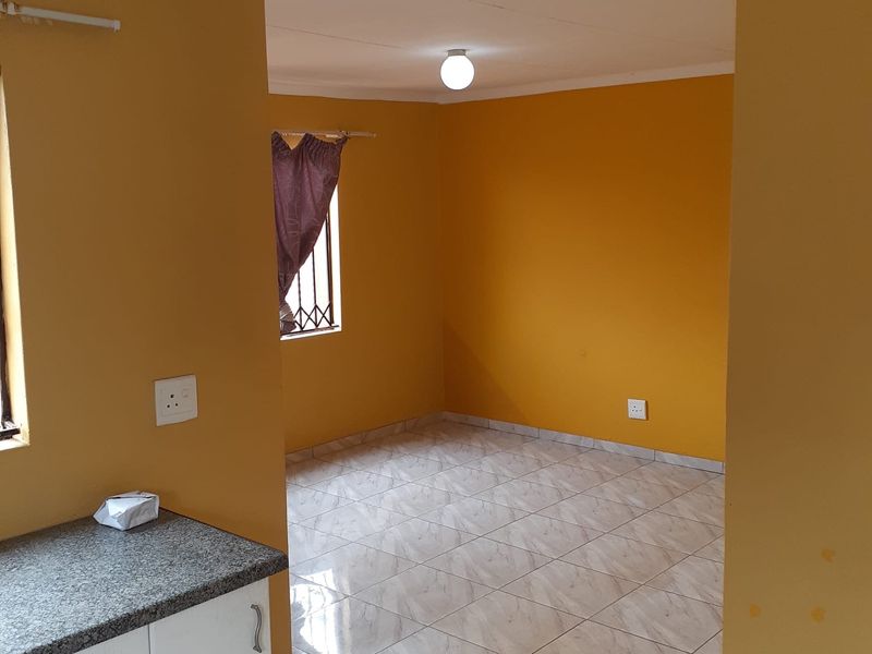 An open-plan office space featuring tiled flooring, mustard-colored walls, and a small built-in kitchenette area with granite countertops.