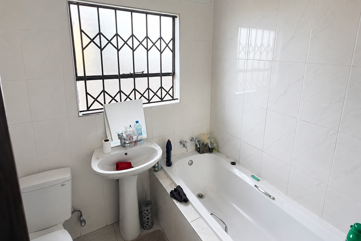 A functional bathroom featuring a pedestal basin, bathtub, and toilet, with tiled walls and a window fitted with a security gate.