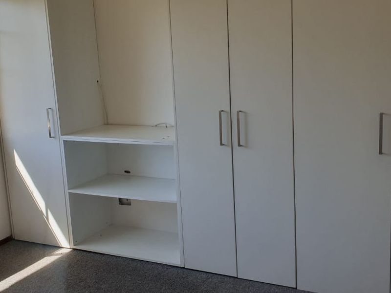 A bedroom featuring extensive white built-in cupboards and integrated shelving, providing ample storage space with natural light from a grid-pattern window.