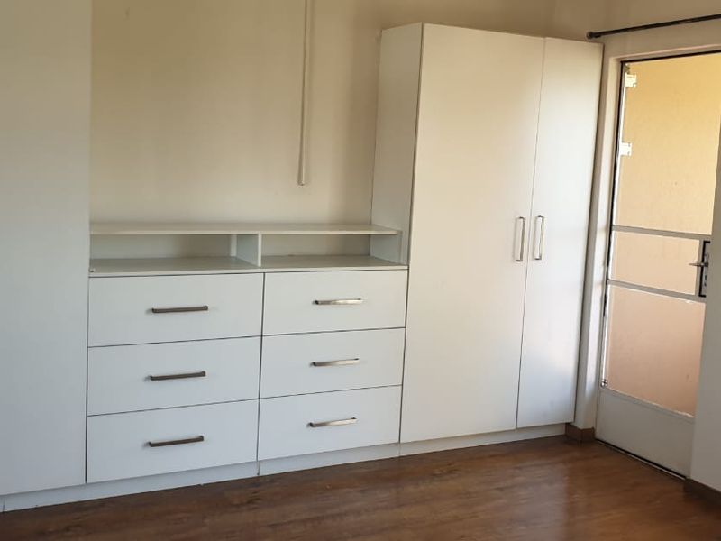 A bright bedroom featuring extensive built-in cabinetry, laminate flooring, and direct access to an outdoor area through a secure door.