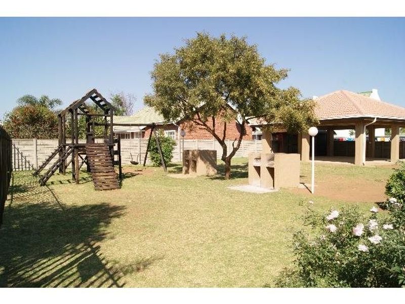 A communal garden area featuring a built-in braai, a covered patio structure, and a children's play area within a fenced residential complex.