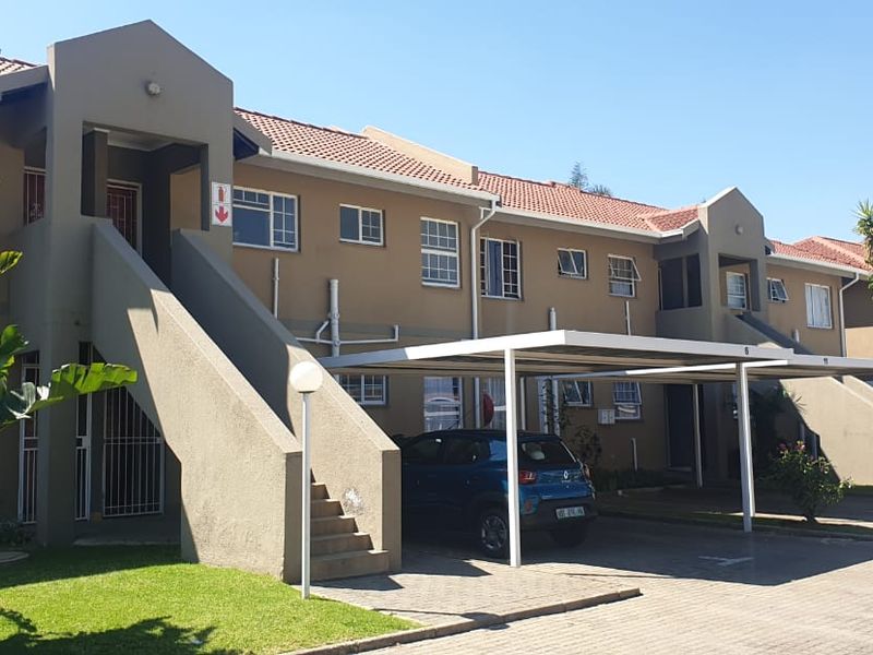 Front elevation of a townhouse complex featuring a tiled roof, concrete staircases, and covered carport parking bays.
