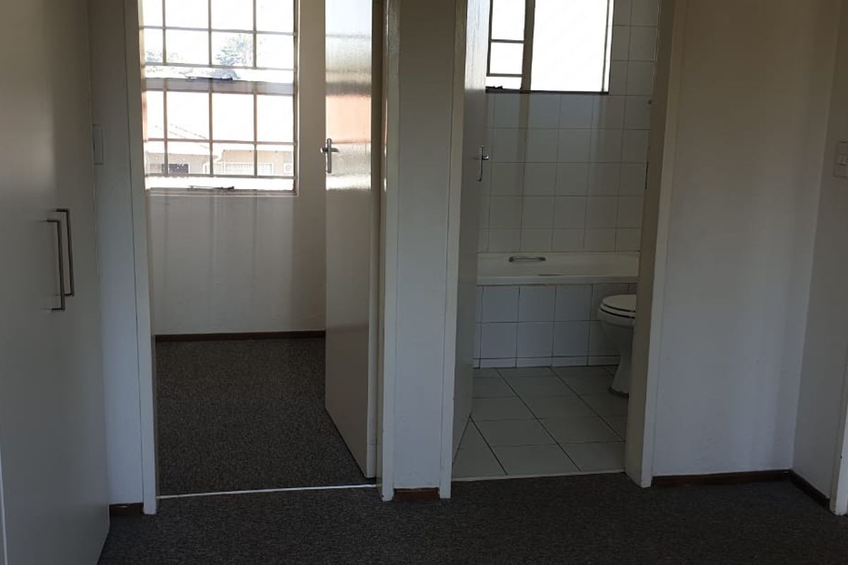 An empty bedroom featuring built-in cupboards and an attached en-suite bathroom with a bathtub.