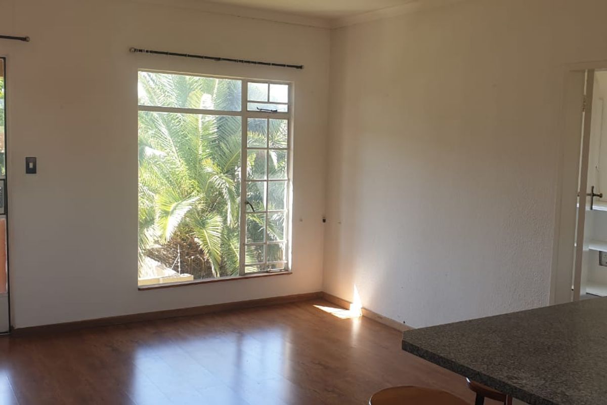 Spacious open-plan living area featuring laminate flooring, large windows for natural light, and a functional kitchen counter, offering a blank canvas for personalization.