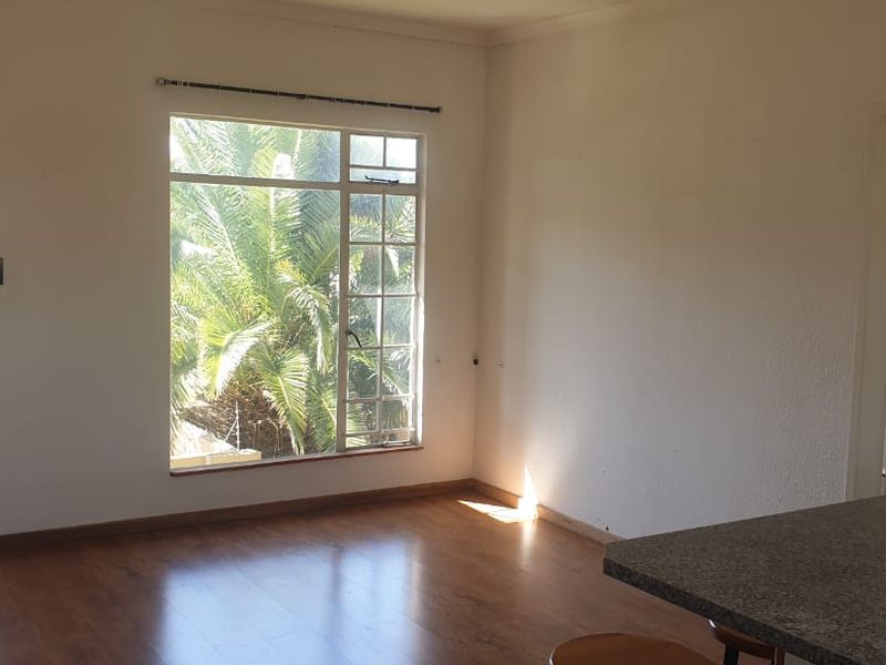 Spacious open-plan living area featuring laminate flooring, large windows for natural light, and a functional kitchen counter, offering a blank canvas for personalization.
