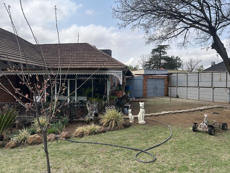 Rear view of the property featuring a tiled roof, decorative ironwork detailing, a spacious garden, and a detached garage structure.